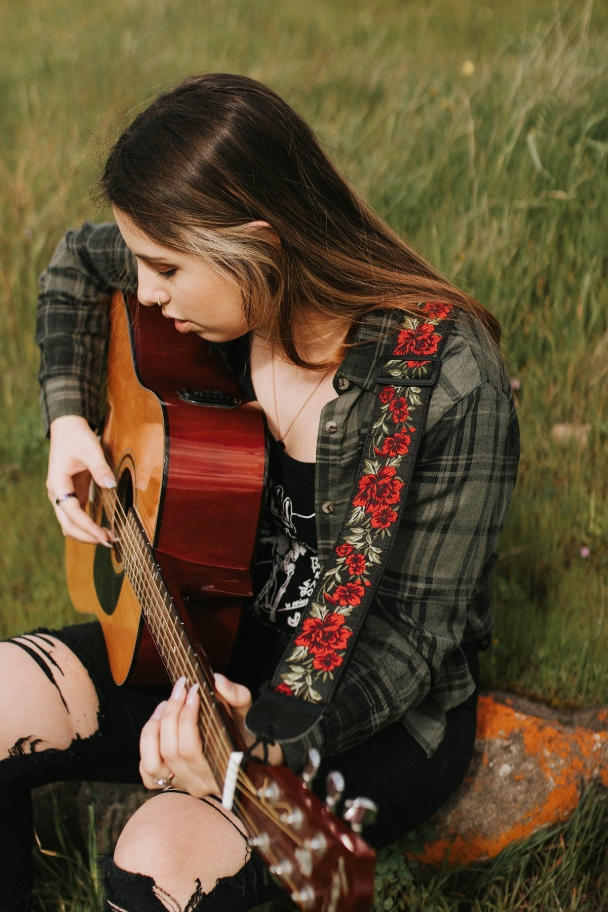 a girl playing an acoustic guitar with a red roses guitar strap